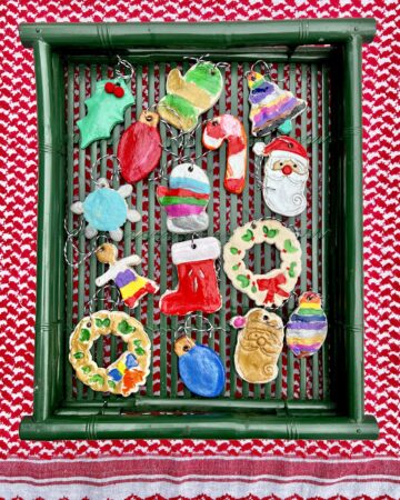 Painted salt-dough christmas ornaments on a green tray on red and white cloth