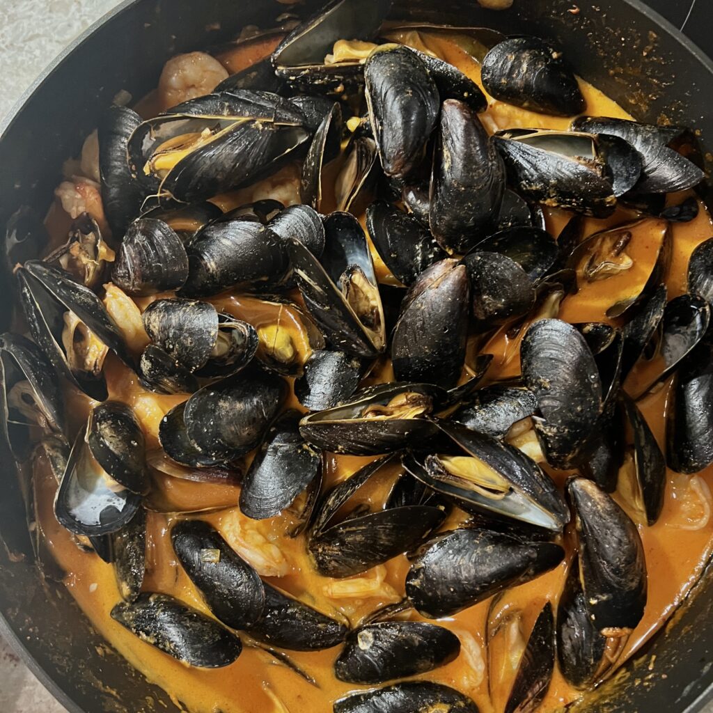 Mussels and shrimp in red curry coconut sauce in skillet showing mussels opened