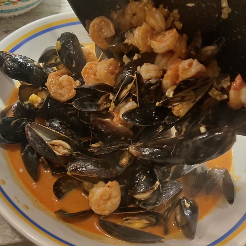 Shrimp and Mussels in Red Curry Sauce being poured from skillet into serving dish
