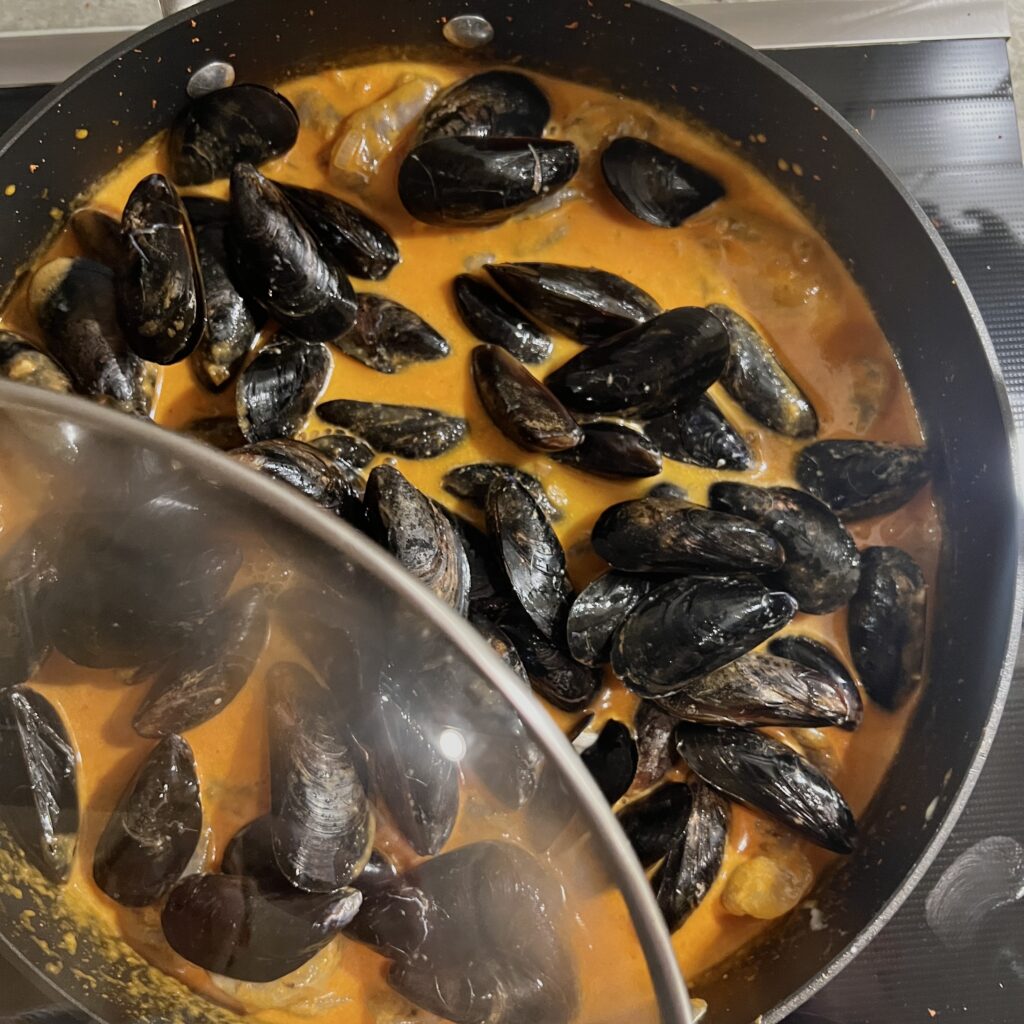 Mussels and Shrimp in a red curry coconut sauce in skillet with lid partially open