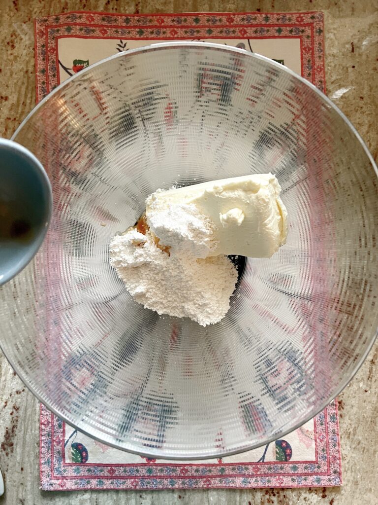 small bowl pouring vanilla into bowl of cream cheese and powdered sugar
